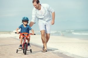 father and son learning to ride a bicycle at the beach having fun together